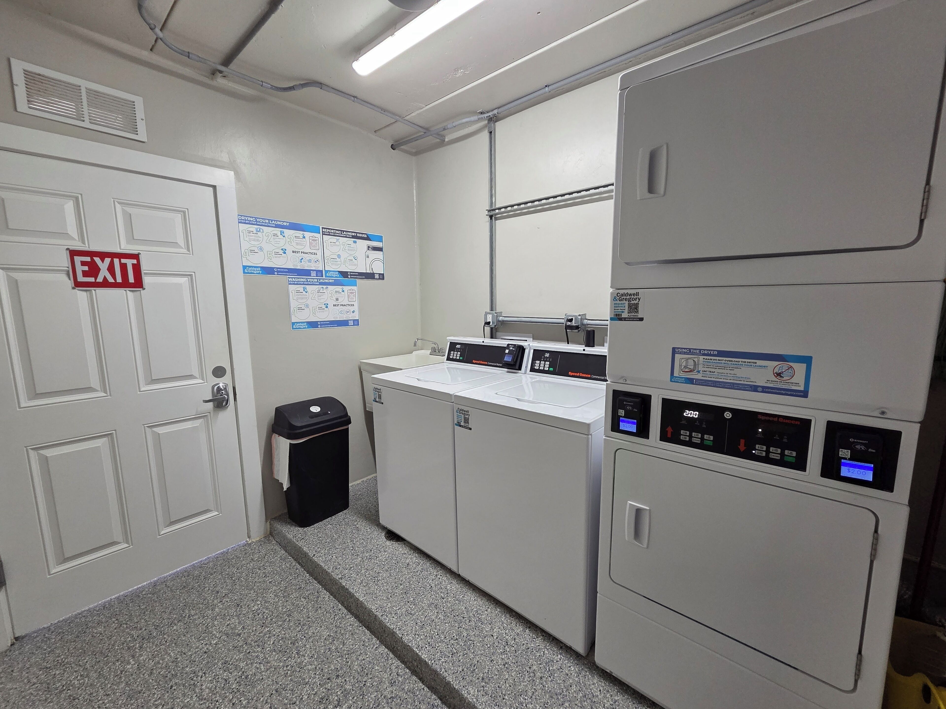 Una sala de lavandería con una puerta de salida, un cubo de basura y una lavadora.