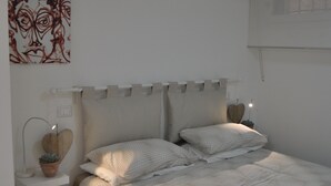 Un dormitori amb un llit, taules de nit, una làmpada penjada a la paret i un ventilador de sostre.