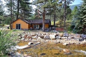 View of side of cabin from across river. Patio, hot tub, fire pit, gas grill.