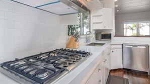 Une cuisine moderne avec des carreaux blancs, des appareils en acier inoxydable et une fenêtre donnant sur des palmiers.