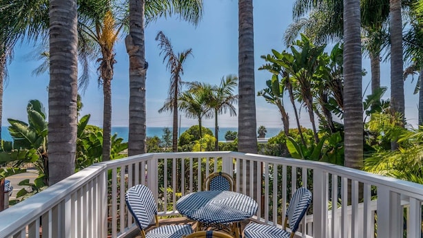 Une terrasse dotée d’une balustrade blanche, d’une table ronde et de quatre chaises avec des assises tissées aux couleurs bleu et blanc.