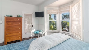 Une chambre à coucher comprenant un lit, une commode en bois, une petite table, un téléviseur et une baie vitrée donnant sur un paysage.