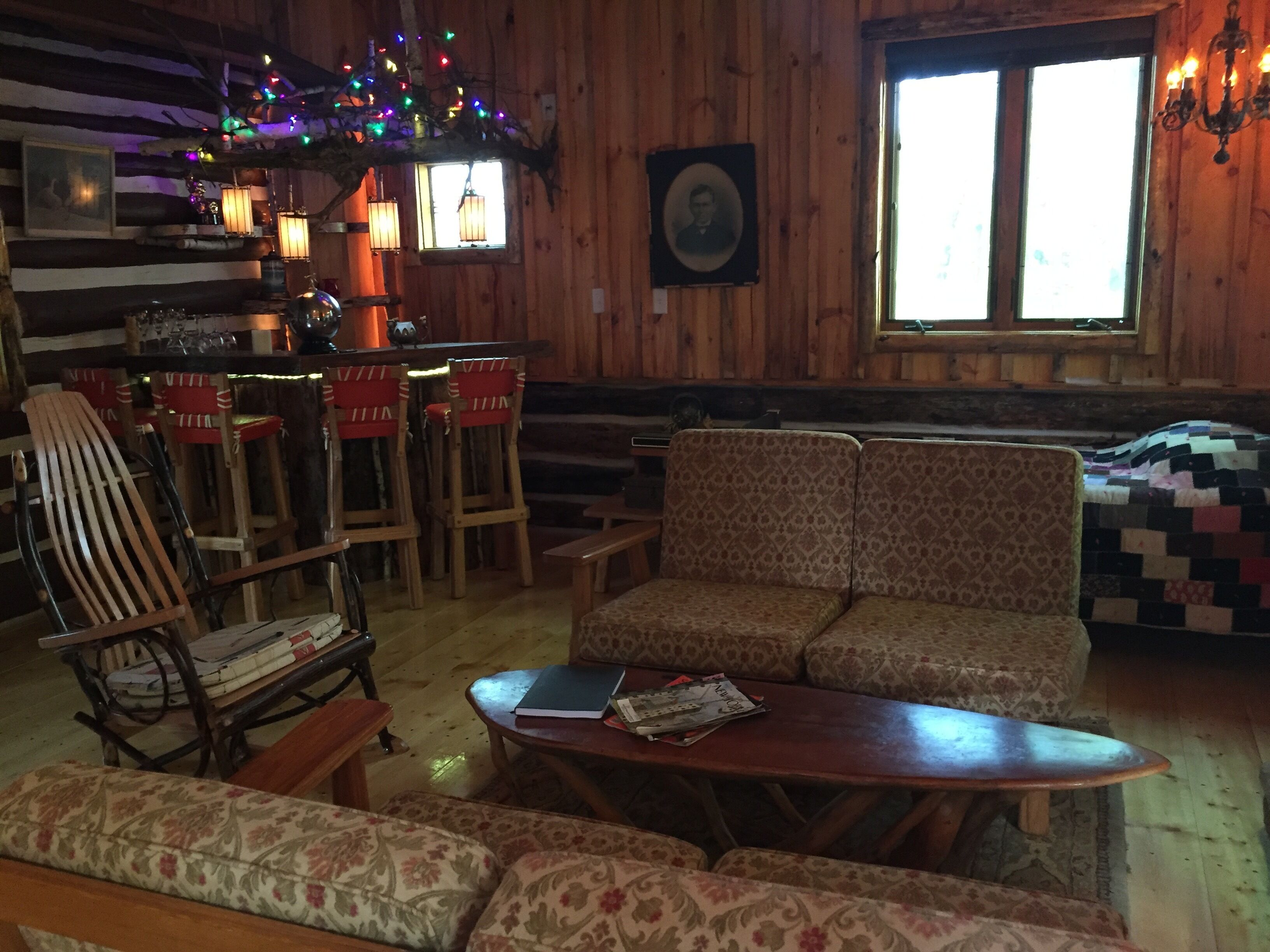 L’intérieur chaleureux d’un chalet avec des murs en bois, une table à manger en bois, des chaises rouges, un canapé à motifs et une fenêtre offrant une belle vue.
