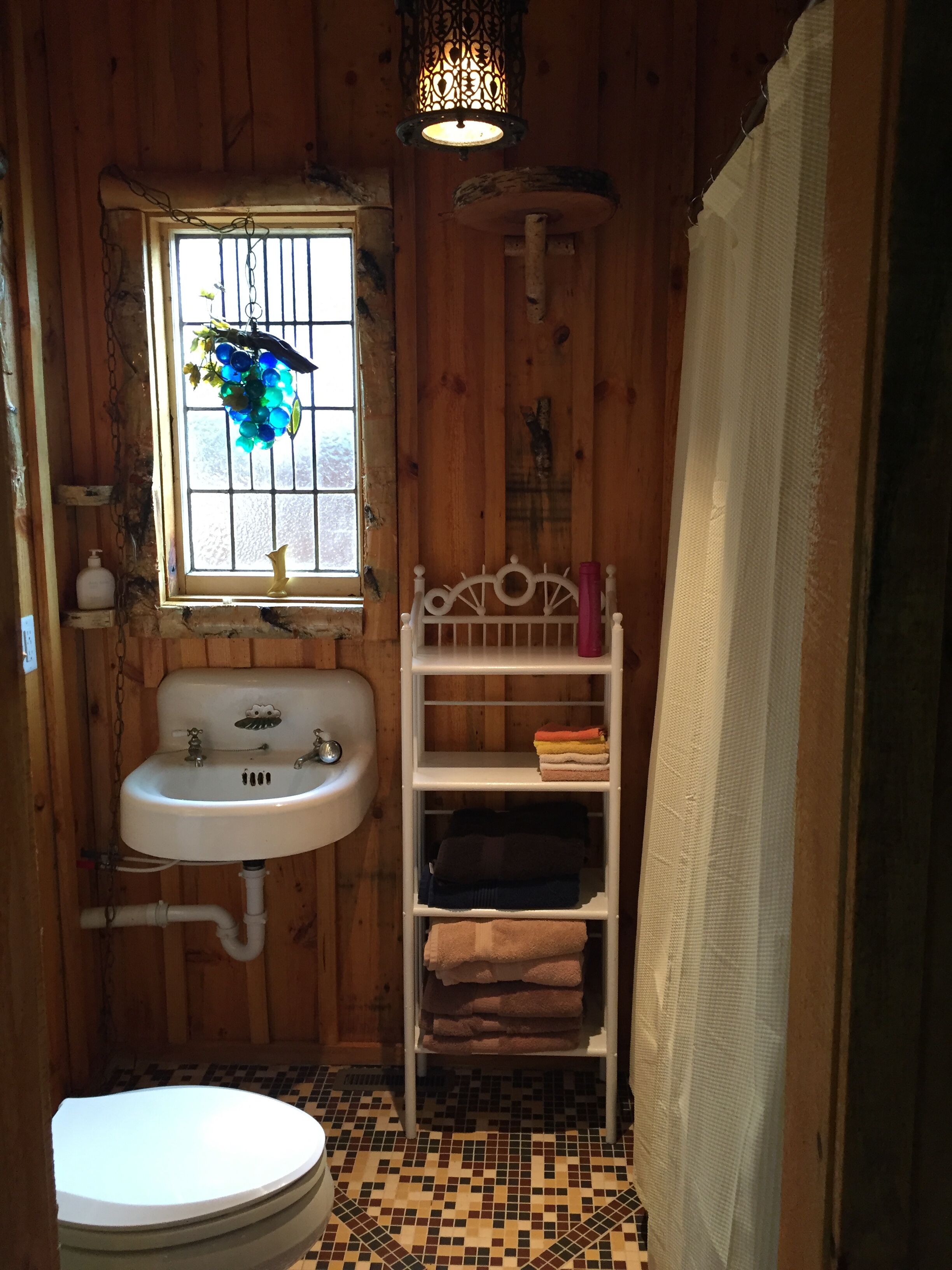 Un bagno piccolo e rustico con arredi in legno, un lavandino bianco, una finestra con una pianta, uno scaffale con asciugamani e un water.