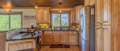 Una cocina con armarios de madera, un refrigerador de acero inoxidable, horno empotrado y encimera de piedra.