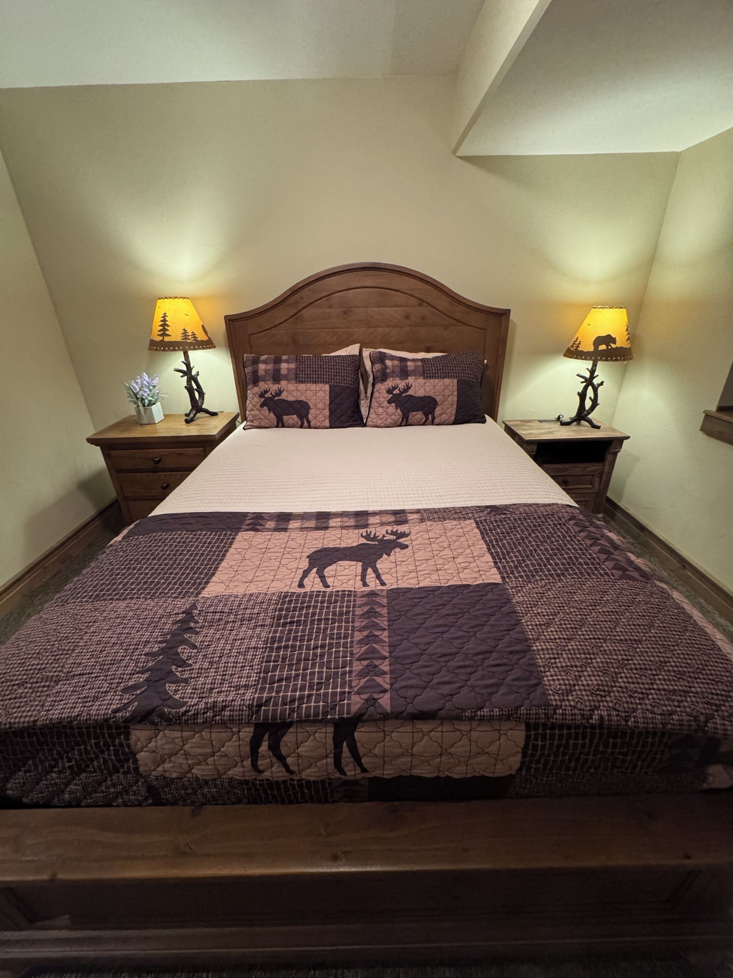 A bed with a patterned quilt, two bedside lamps, and a wooden headboard.