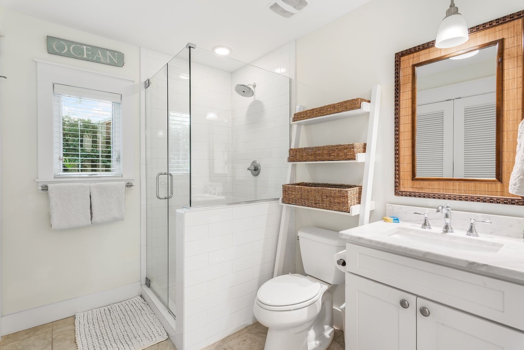 Een moderne badkamer met een douche met glazen wand, een wit toilet en een wastafel met een spiegel en planken.
