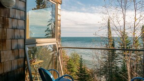 Une cabane en bois dotée d’un balcon en verre donnant sur un lac et une forêt.