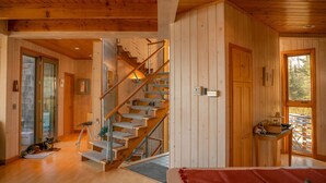 Un intérieur en bois avec un escalier, un chien et une vue par la fenêtre.