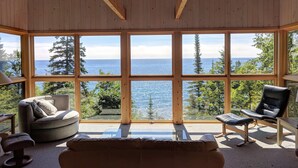 Une pièce dotée de grandes fenêtres donnant sur la mer et les arbres. On y trouve un canapé, un fauteuil et une petite table.