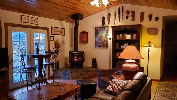A cozy living room with a fireplace, wooden furniture, and various decorations. - Beautiful Creekside Home in Mariposa Pines Close to Yosemite.  No cleaning fee.  (Mariposa)