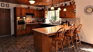 A kitchen with wooden cabinets, a central island with bar stools, stainless steel appliances, and a patterned floor. - Beautiful Creekside Home in Mariposa Pines Close to Yosemite.  No cleaning fee.  (Mariposa)