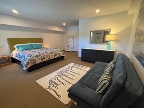 A bedroom with a bed, a sofa, a desk, and a mirror.