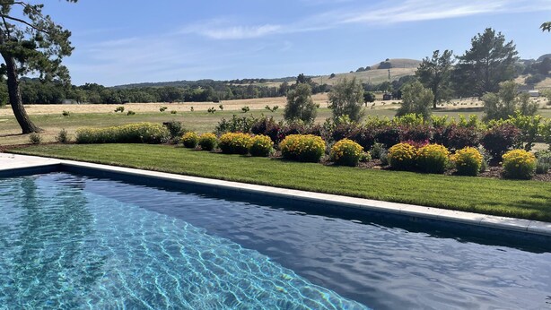 Piscina cristalina con vistas a un jardín ajardinado y colinas lejanas.