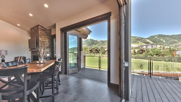 Una cocina moderna con una pared de acento de piedra, un comedor con una mesa y sillas de madera, y un balcón con vistas al paisaje circundante.