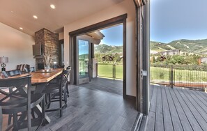 Una cocina moderna con una pared de acento de piedra, un comedor con una mesa y sillas de madera, y un balcón con vistas al paisaje circundante.