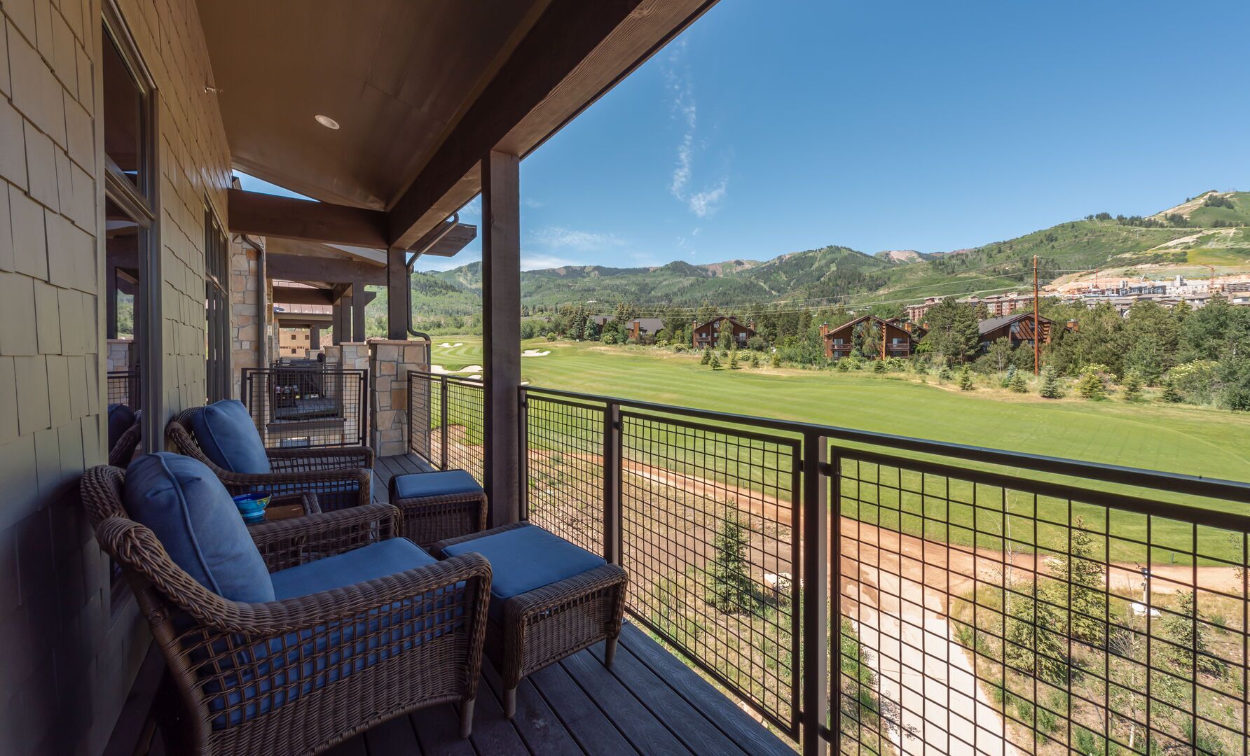A balcony with wicker furniture overlooking a golf course and residential buildings.