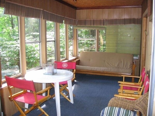 Una habitación acogedora con una mesa redonda, dos sillas de madera, un banco acolchado y amplias ventanas con vistas al verdor.