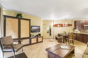 Een woonkamer met een televisie, een houten eettafel en een keukenhoek met een magnetron.