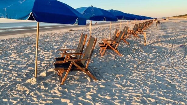 En strand med rækker af træsolstole og blå parasoller.
