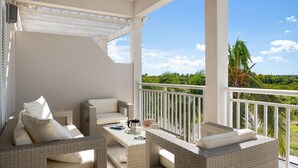 A balcony with wicker furniture, a white railing, and a view of greenery. - Updated Stunning Ocean Club Plaza luxury family spacious top floor apartment  (Providenciales)