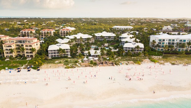 A resort with multiple buildings, a beach with umbrellas, and a clear view of the ocean. - Updated Stunning Ocean Club Plaza luxury family spacious top floor apartment  (Providenciales)