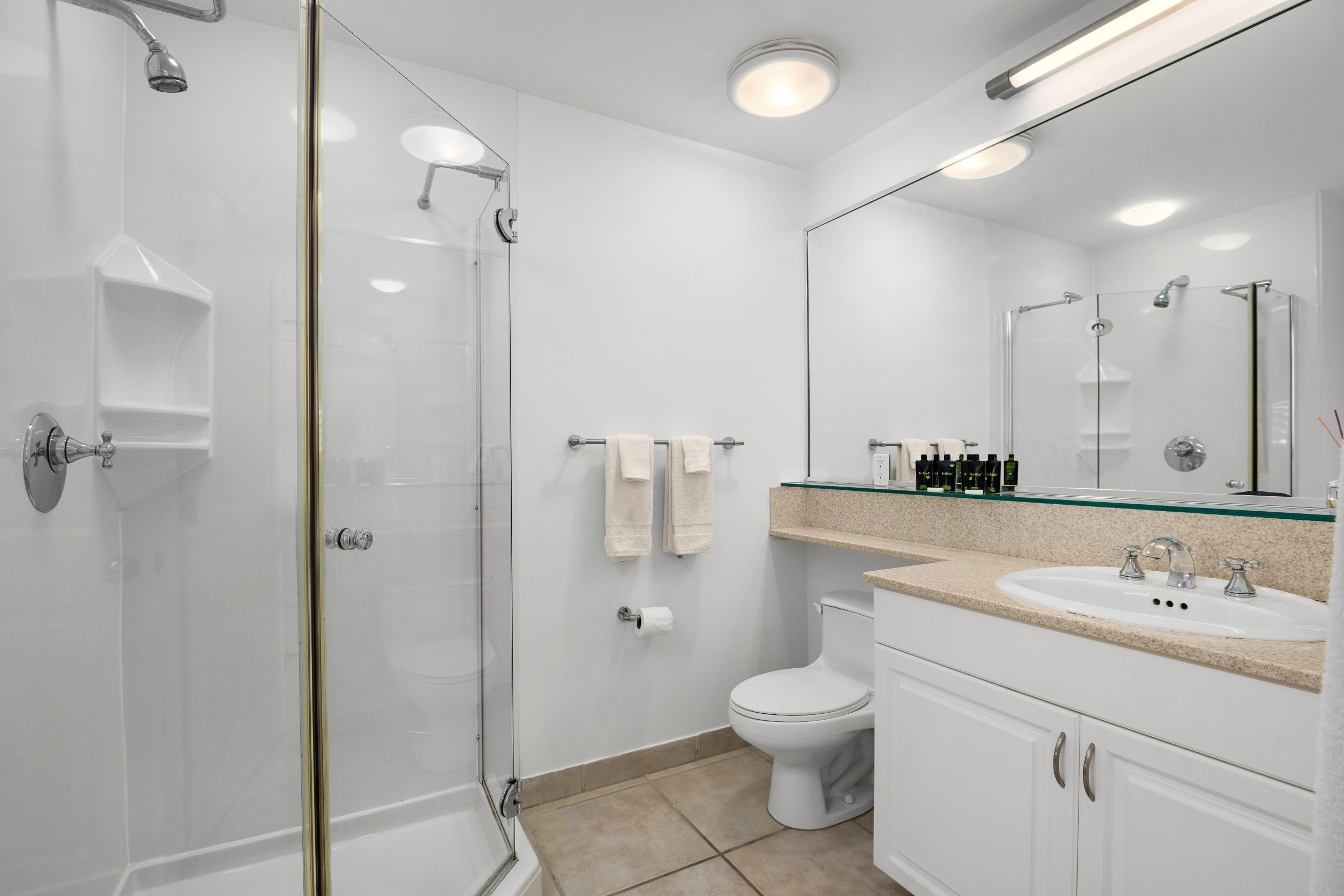A modern bathroom with a glass-enclosed shower, a white toilet, and a sink with a glass countertop.