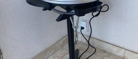 Ein tragbarer Grill mit schwarzem Gestell und silbernem Deckel, beschriftet mit "GEORGE FOREMAN", steht auf einem gefliesten Boden vor einer weißen Wand.