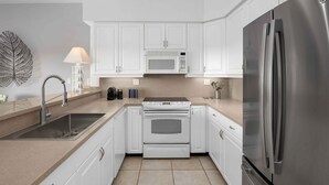 A modern kitchen with white cabinets, a stainless steel refrigerator, a microwave, and a built-in oven. - Updated Stunning Ocean Club Plaza luxury family spacious top floor apartment  (Providenciales)