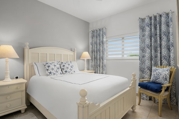 Une chambre à coucher avec un lit, des tables de chevet, une chaise et des rideaux.