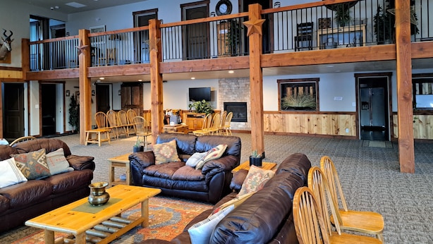 Eine geräumige Lobby mit hoher Decke, Holzbalken, einem Kamin und einem Balkon im zweiten Stock mit Geländern.