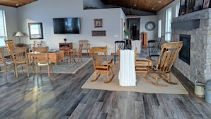 Ein geräumiges Wohnzimmer mit hohen Decken, Holzboden, Kamin und Wandfernseher.