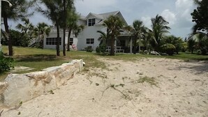 Ein Strandgrundstück mit einem großen Haus, Palmen und einer Sandfläche.