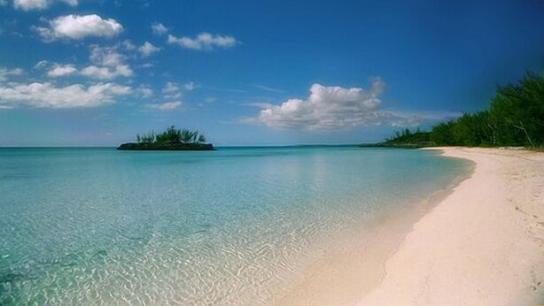 Ein klares türkisfarbenes Meer, ein Sandstrand und eine kleine Insel mit Vegetation.