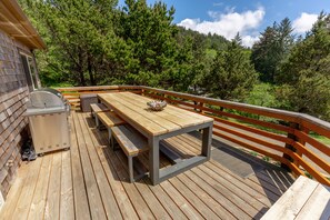 A wooden deck with a table and benches, a grill, and a trash can.