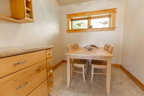 A kitchen with wooden cabinets, a dining table, and chairs. There is a window with a view of trees and birds. - Headland- Oceanfront Family Friendly (Gold Beach)