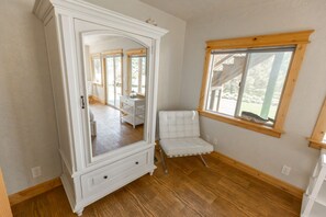 A room with a large white armoire, a white upholstered chair, a wooden window sill, and a view of an outdoor area.