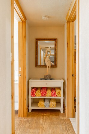 A hallway with a white console table, a mirror with a decorative frame, and shelves with rolled towels. - Headland- Oceanfront Family Friendly (Gold Beach)