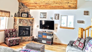 A cozy living room with a stone fireplace, a flat-screen TV, and a wooden ceiling. - Relax with Family, Friends and Dogs, in a Secluded 4b/3b Cabin in the Woods (Fairplay)