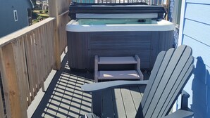 Un bain à remous sur une terrasse en bois, agrémentée de chaises Adirondack.