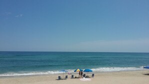 Une plage avec un ciel dégagé, une mer calme, des chaises de plage et des parasols.