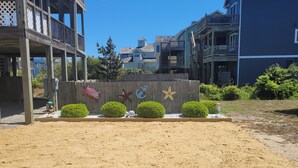 Une plage de sable bordée d’une clôture en bois décorée de motifs représentant des étoiles de mer et des ancres.