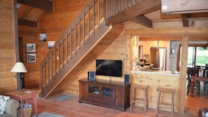 Un interior de madera con una escalera, un televisor sobre un mueble y una zona de cocina.