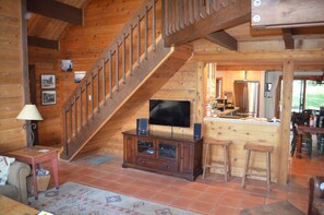 Cozy cabin interior with a staircase, flat-screen TV, and kitchen area.