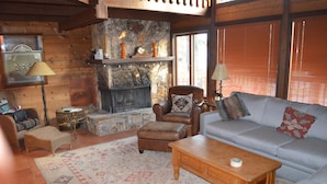 Una sala de estar acogedora con chimenea de piedra, un sillón de cuero y un sofá gris.