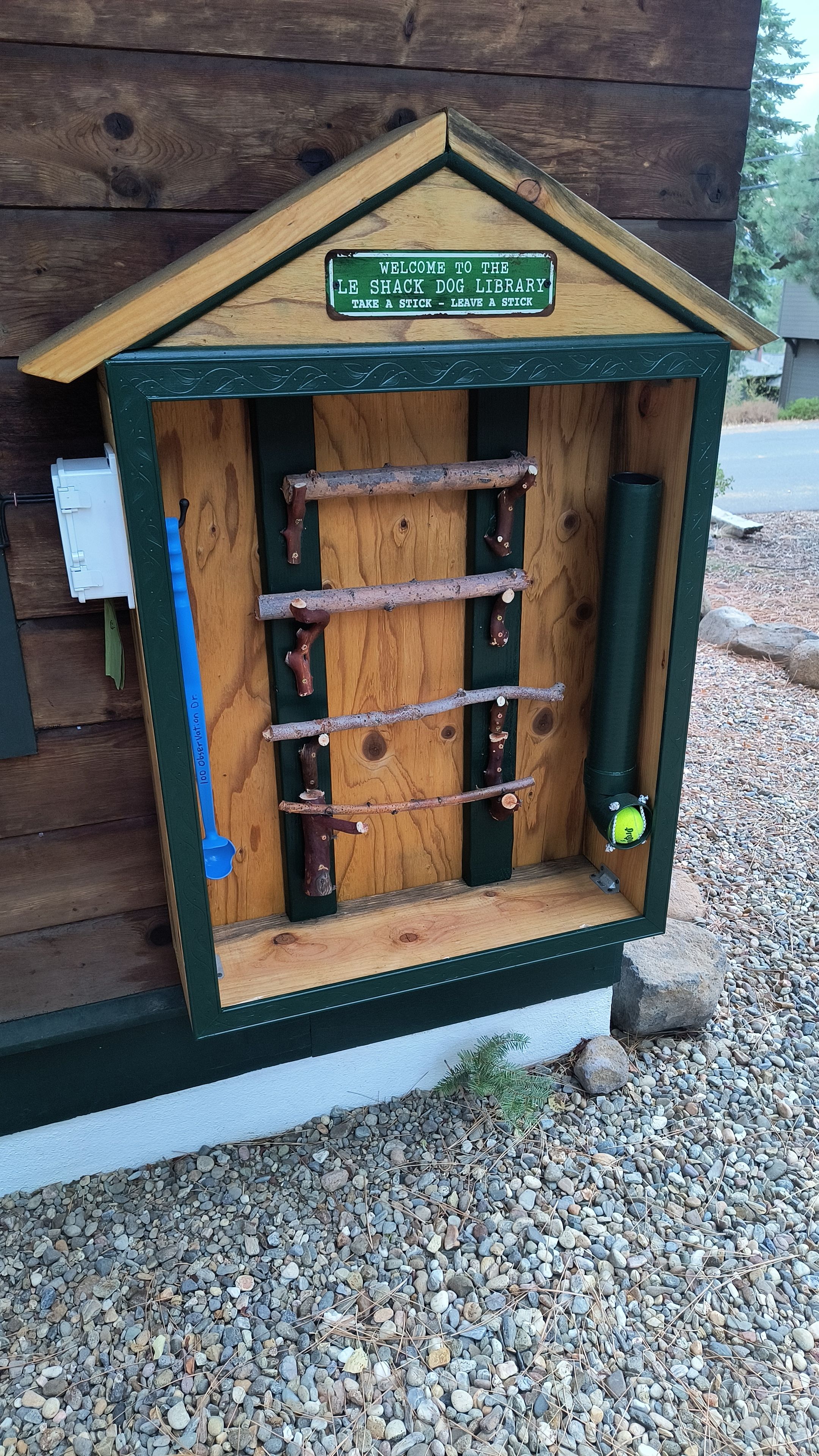 Eine Holz-Hundebibliothek mit einem Schild, auf dem 'Welcome to the Le Shack Dog Library' steht, und einem Stockhalter im Inneren.