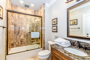 A modern bathroom with a glass-enclosed shower, a white toilet, a marble sink, and a large mirror.
