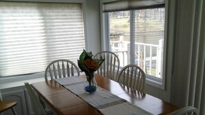 A dining table with a vase of flowers, white chairs, and a view of a deck and trees through the window. - Heaven Can't Wait, On Beautiful Kinderhook Lake!! (Valatie)