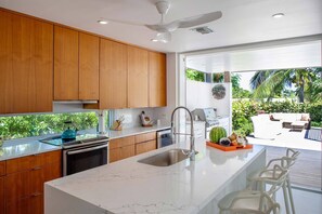 Enjoy meals and relaxation in this kitchen with a large island, sink, and bar seating, overlooking a lush outdoor area with patio and seating.