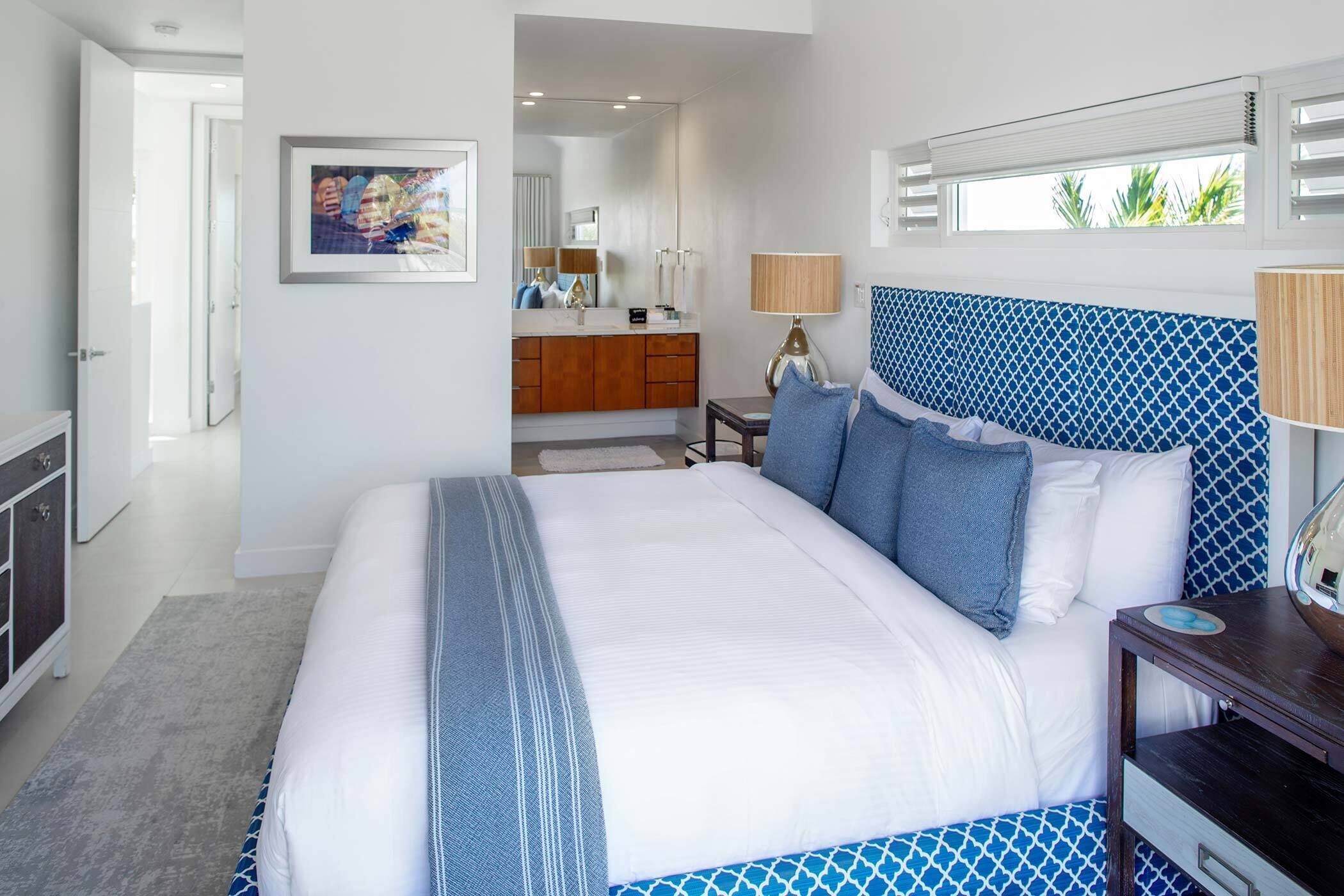 Une chambre à coucher avec un grand lit, une commode, une coiffeuse avec un miroir et une fenêtre avec des stores.